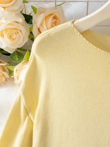 Dettaglio della trama a maglia fine e dello scollo rotondo su un maglione giallo donna
