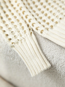 Dettaglio ravvicinato della trama a maglia traforata e del polsino a coste sul cardigan