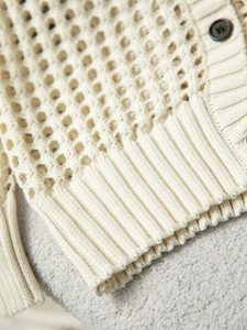 Dettaglio del cardigan in maglia traforata con orlo a coste e bottone marrone scuro