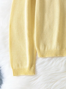 Dettaglio del maglione in maglia giallo tenue con trama fine e polsini a costine fini