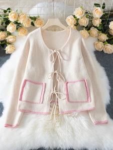Detail of beige knit cardigan with soft ribbon bow ties and contrast pink trim