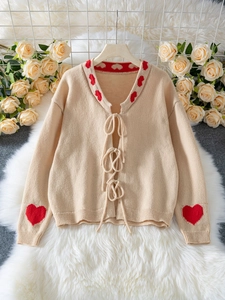 Detail of apricot knit cardigan featuring red heart patterns and three front ties