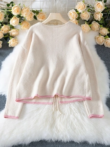Detail of knit cardigan cuffs and hem with contrast pink trim on beige fabric