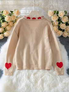 Detail view of the beige knit cardigan back with red heart patterns on cuffs and collar