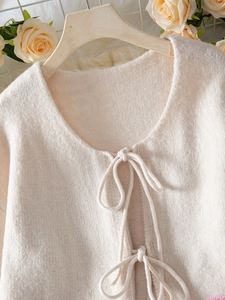 Detail of soft cream knit cardigan showing delicate texture and front tie closures