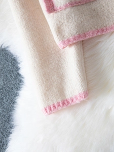 Detail of cream knit cardigan featuring pink contrast edges and ribbed texture finish