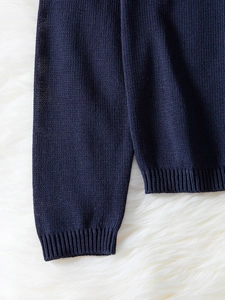 Dettaglio dei polsini e dell'orlo a costine su un maglione blu scuro in maglia fine