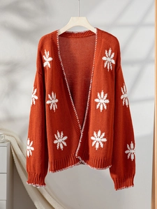 Detailed close-up of white snowflake jacquard patterns on a burnt orange knit cardigan