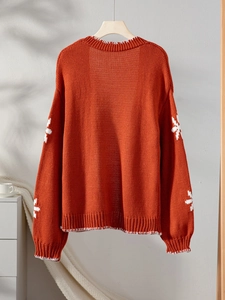 Detail of orange knit cardigan featuring white snowflake patterns and contrast stitching