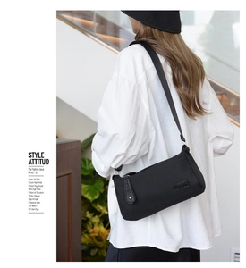 Detail of a black nylon crossbody bag with leather puller shown on a model in a white shirt