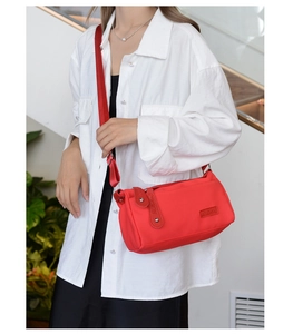 Detail view of a red nylon crossbody bag featuring adjustable straps and silver rivets