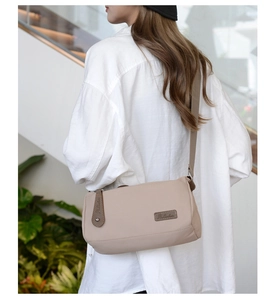 Side view of a beige nylon crossbody bag with adjustable wide strap on white shirt model