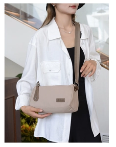 Detail of khaki nylon crossbody bag showing the leather logo patch and wide woven strap