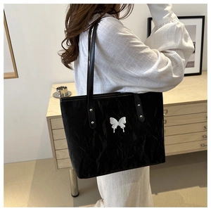 Detail of black tote bag with unique pleated leather texture and silver butterfly emblem