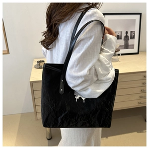 Detail of black pleated tote bag with silver butterfly charm worn over shoulder