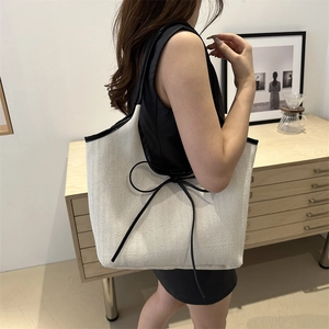 Minimalist cream canvas tote bag with black leather trim and bow detail on a model