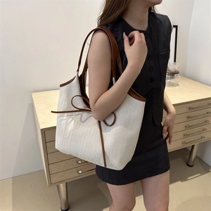 Minimalist beige canvas tote bag with brown leather trim and bow detail shown on shoulder