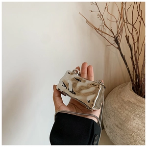 Detail of silver wavy mini chain bag held by hand, showing shiny mirror finish and texture