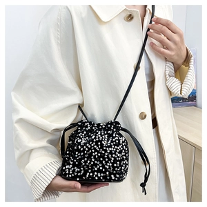 Détail du sac seau à paillettes argentées avec cordons porté sur un manteau beige