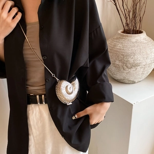 Silver nautilus shell crossbody bag with metal chain shown on a stylish model