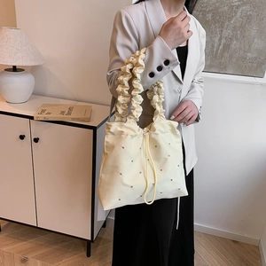 Chic beige tote bag with silver rivets and ruffled shoulder strap shown on a model
