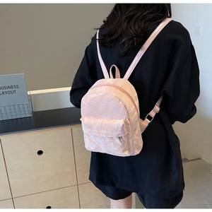 Detail showing the light pink mini backpack with glossy wrinkled texture on a female model