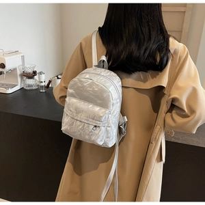 Silver mini backpack featuring unique pleated texture on a modern lifestyle background