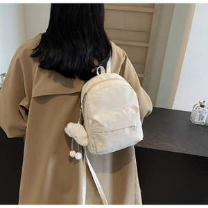 Close-up of white mini nylon backpack featuring front pocket and fluffy cloud keychain charm