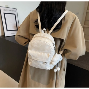 Detail of white mini backpack with crinkled texture and cloud plush charm on model