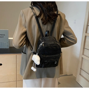 Close-up of black pleated mini backpack with a white plush cloud charm on zipper