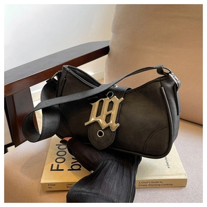 Détail du sac croissant noir avec logo gothique et bandoulière à œillets argentés