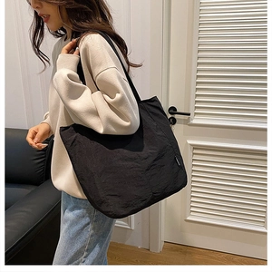 Détail d'un grand sac cabas noir en toile avec étiquette latérale porté par un mannequin