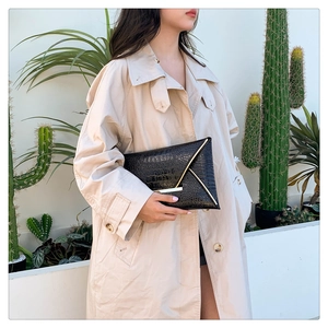 Detail of a chic black crocodile pattern envelope clutch with golden metal trim details
