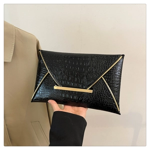 Detail of black crocodile pattern envelope clutch with gold metal trim and glossy finish