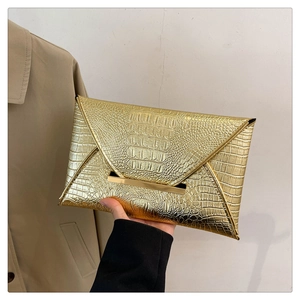 Detail of gold envelope clutch bag with crocodile texture and metallic bar closure