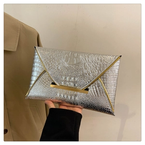 Detail of silver envelope clutch bag with crocodile texture and gold metal bar accents