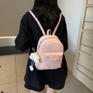 Mini pink backpack with marble texture and cloud pendant worn by a model in soft light