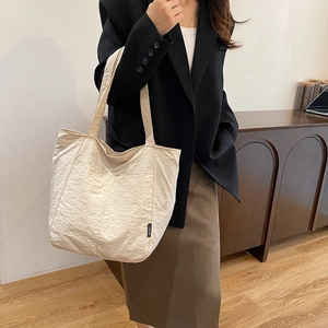 Grand sac cabas plissé beige avec larges bretelles porté par un mannequin au style épuré
