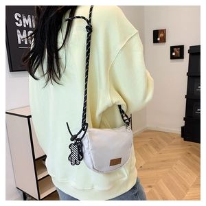 Dettaglio borsa a mezzaluna in nylon crema con tracolla intrecciata e orsetto