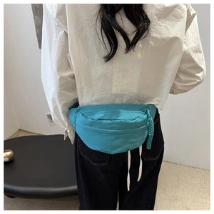 Detail of teal fabric waist bag with crescent shape and woven zipper on model