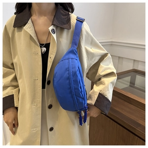 Close-up of bright blue nylon chest bag with woven zippers on a beige trench coat