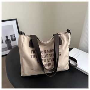 Détail du cabas en toile beige avec poignées en sangle marron foncé et typographie imprimée
