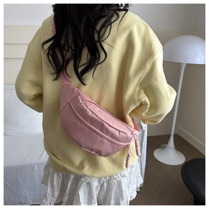 Detail view of pink crossbody chest bag showing zippers and woven cord pullers on a model