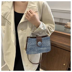 Détail du sac à bandoulière en denim bleu avec rabat en cuir brun et chaîne argentée