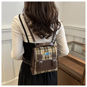 Detail of vintage plaid backpack showing brown leather flap with dog embroidery