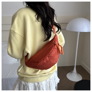 Detail of an orange canvas crescent chest bag shown worn over the shoulder on a model