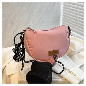 Dettaglio di una borsa a mezzaluna rosa in nylon con tracolla intrecciata e ciondolo a orsetto