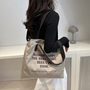 Grand sac cabas beige en toile avec texte noir et anses marron porté par un mannequin