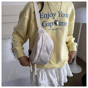 Detail of a beige canvas waist bag featuring a wide adjustable strap and woven zipper pull