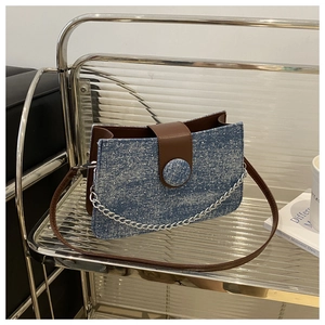 Gros plan d'un sac bandoulière en denim scintillant bleu avec rabat en cuir marron et chaîne